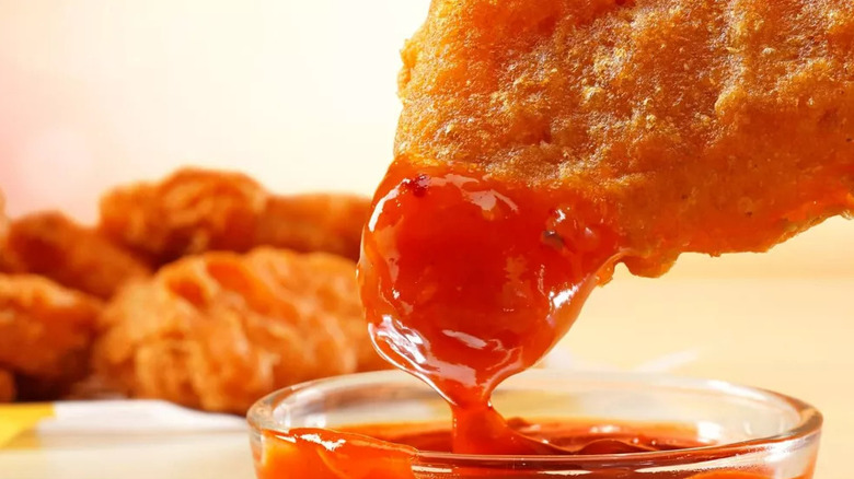 Spicy McDonald's chicken mcnugget being dipped in spicy sauce