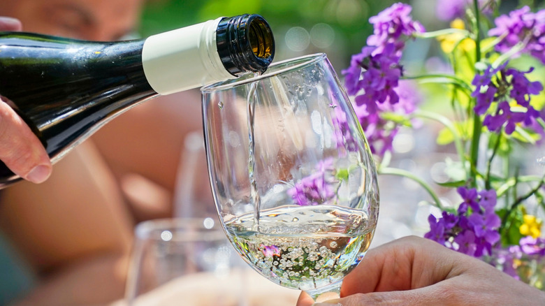 Hand pouring wine from bottle into a glass outdoors with flowers in background