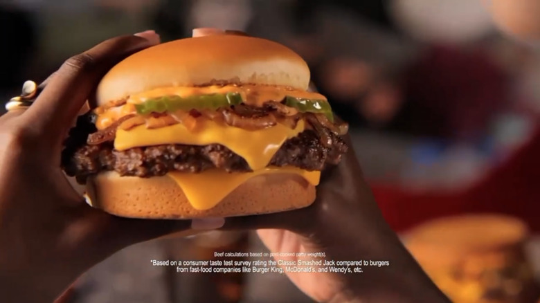 Screen grab from a commercial featuring two hands holding a smashed jack from Jack In The Box