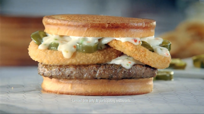 A burger with pepperjack cheese, jalapeño peppers, and onion rings on sourdough bread