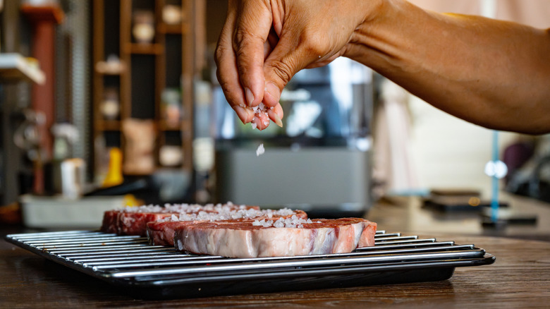Hand sprinkling coarse salt on steak