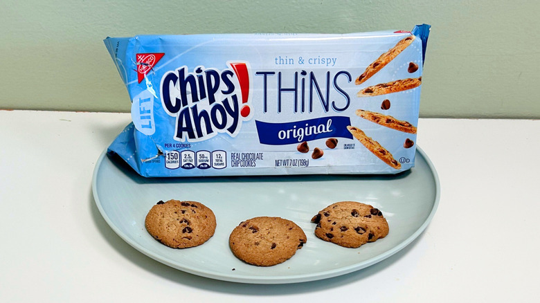 Three cookies on a plate with a bag of Chips Ahoy! Thins Original