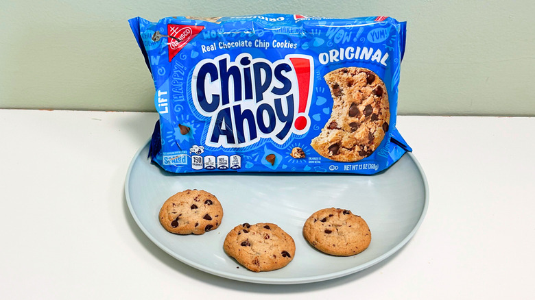 Three cookies on a plate with a bag of Chips Ahoy! Original