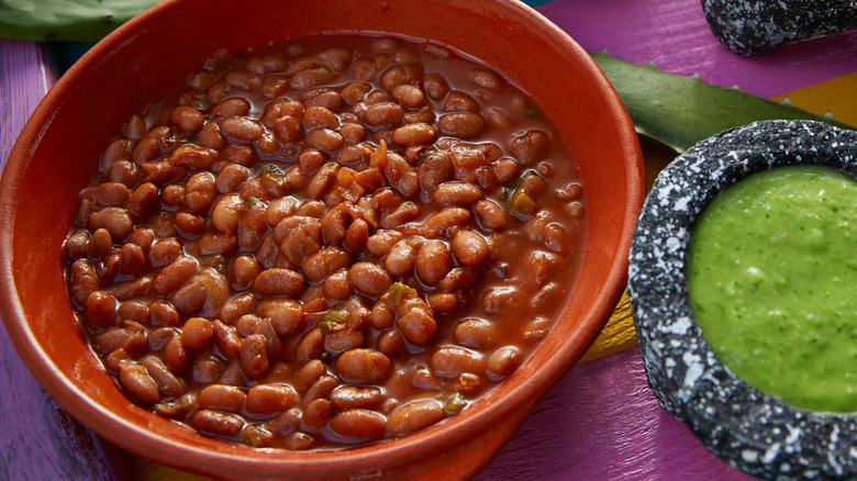 Overhead view of a terra cotta bowl of beans next to a bowl of green sauce