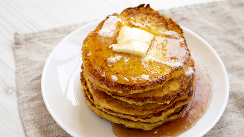 A pile of cornmeal Johnnycakes on a plate, topped with butter and syrup