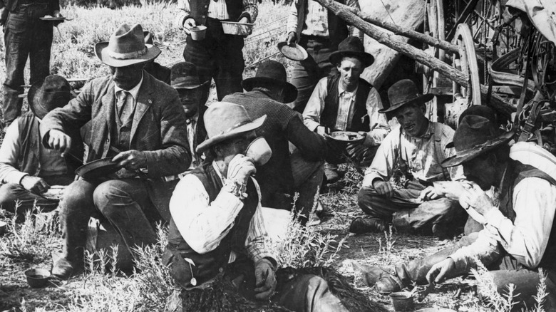 A vintage photo of cowboys eating around a chuckwagon