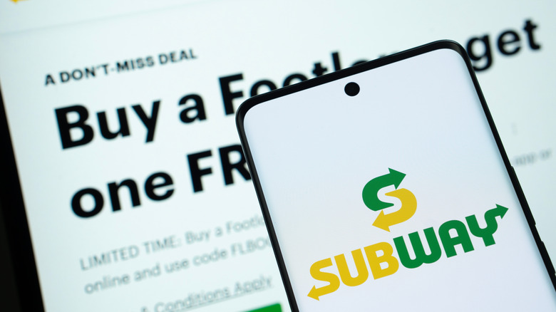Phone screen with Subway logo in foreground, coupon offer for BOGO sandwich on screen in background