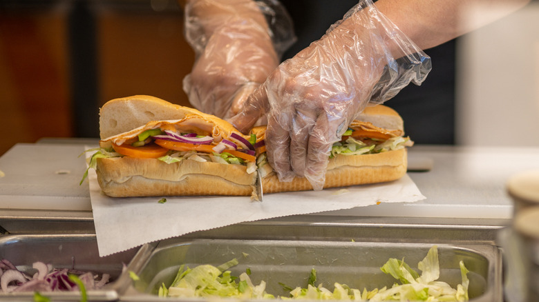 Subway employee slicing sandwich in half