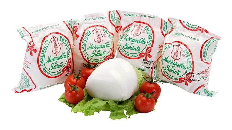 4 sealed packets of mozzarella, with a ball of mozzarella sitting on a bed of lettuce with whole tomatoes on each side