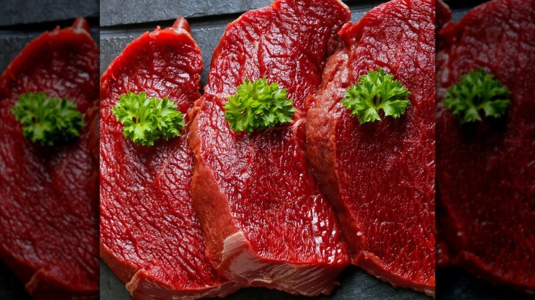 Three slices of uncooked elk meat with green garnish on top