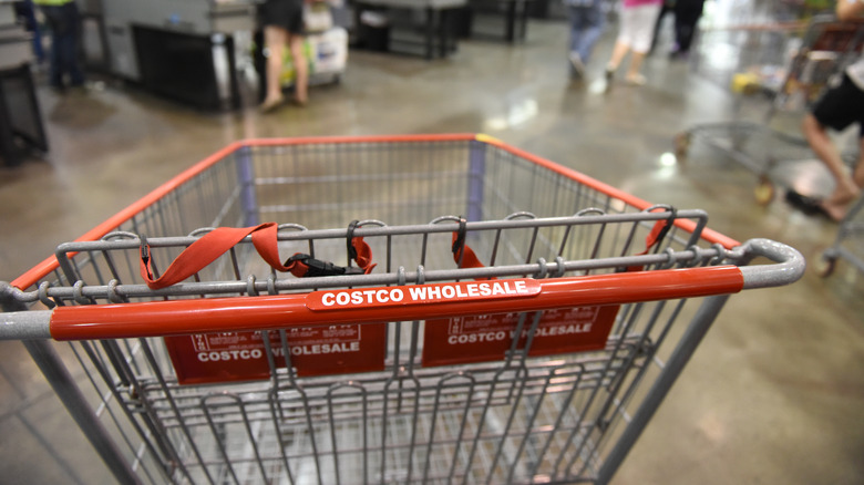 Metal Costco cart with red handle with the text "Costco Wholesale" with check out aisles in background