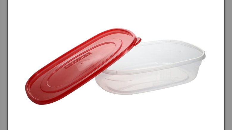 A McCormick Rectangular Storage Container with a red lid resting on its side on a white background