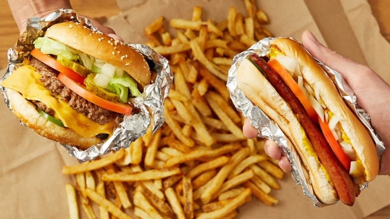 Two hands holding a Five Guys burger and sandwich over a pile of fries