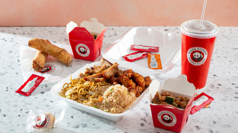 Panda Express plate surrounded by side takeout dishes, sauces, drink, and egg rolls