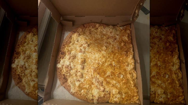 A pizza in its delivery box with the cheese slipping off