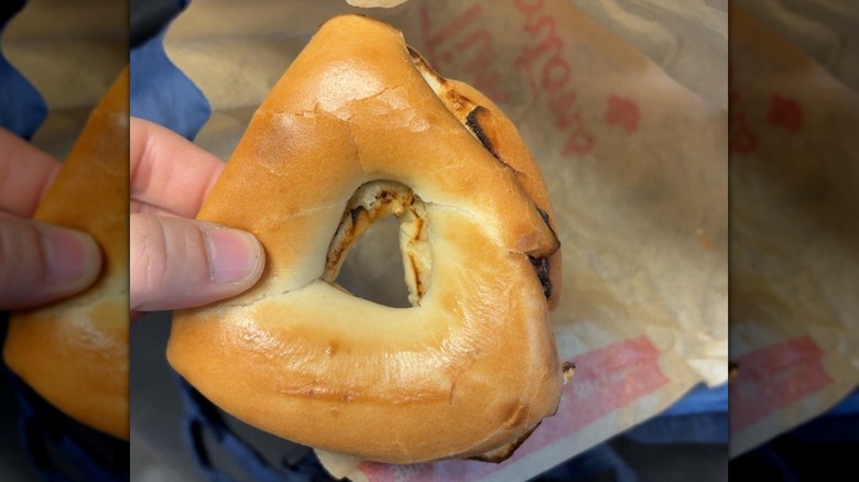A finger and thumb holding a triangular bagel