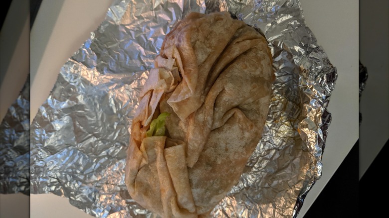 A large, badly wrapped, oval burrito on silver foil