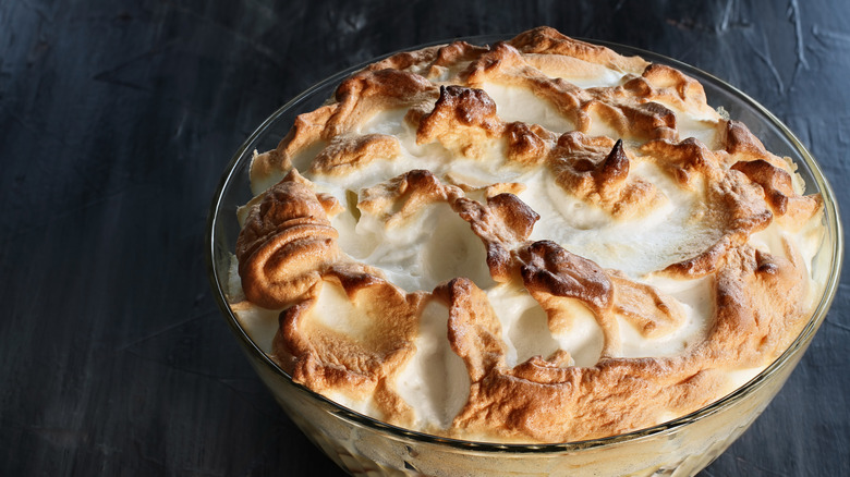A bowl of banana pudding with toasted meringue in a glass bowl against a dark colored background