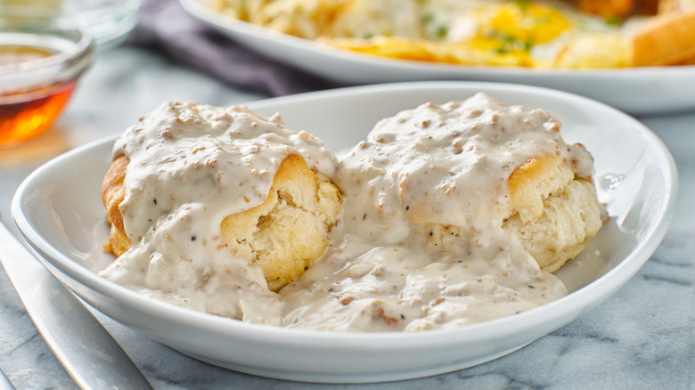 2 biscuits topped with white gravy in a white bowl.