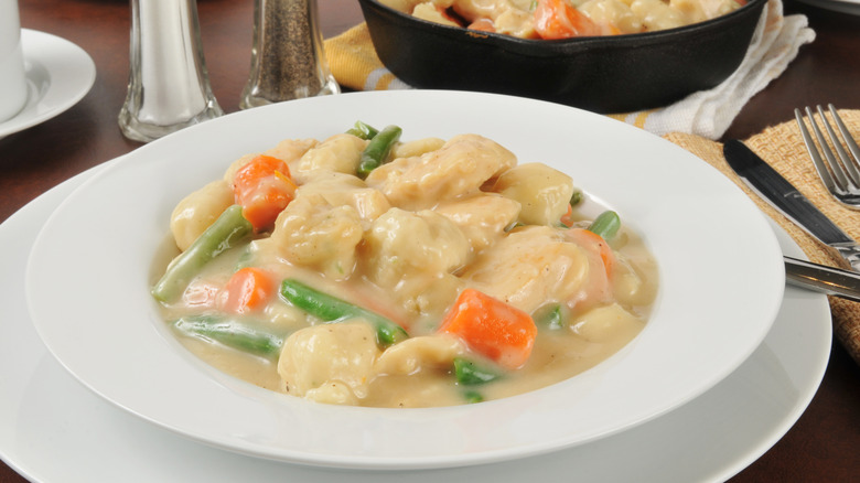 A bowl of Southern-style chicken and dumplings in a white bowl on a white charger plate.