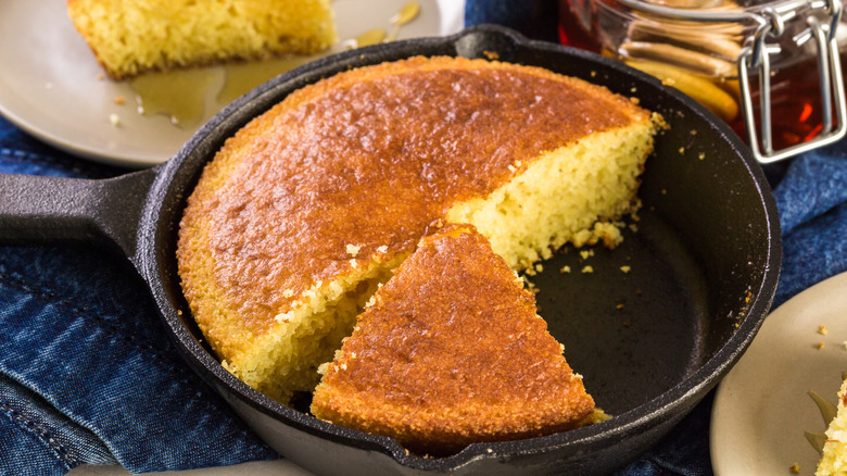 Cast iron pan with sliced cornbread in a denim tablecloth with assorted plates around it.