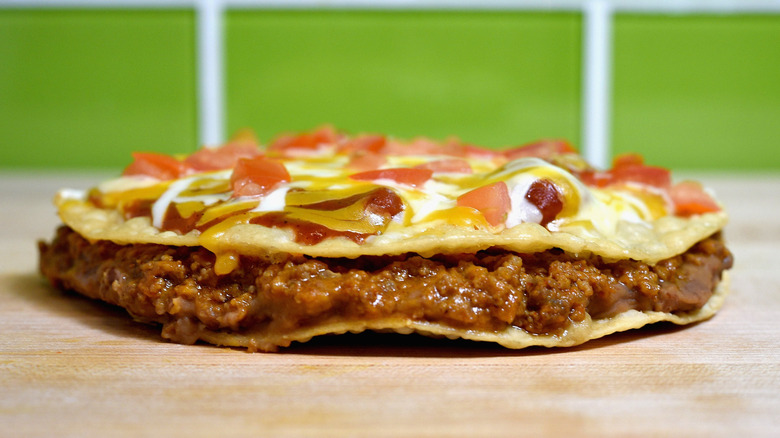 A Taco Bell Mexican Pizza on a wooden table with a green background