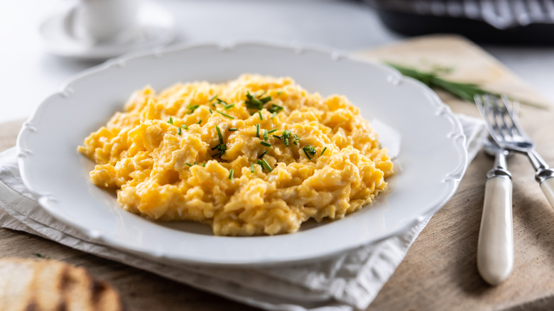 A plate of scrambled eggs on a white plate on a table with a napkin and cutlery
