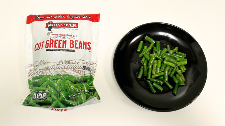 A black plate of green beans next to a bag of Hanover Cut Green Beans