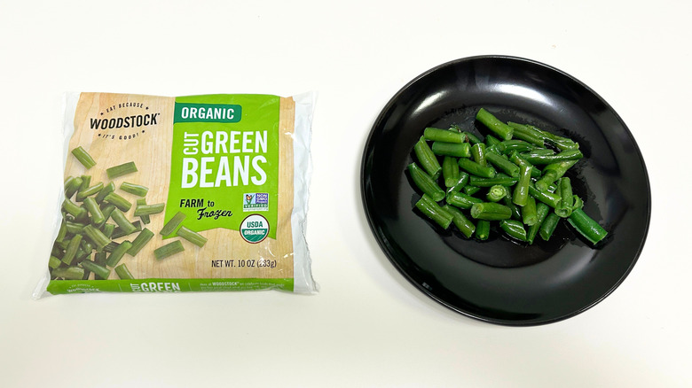 A black plate of green beans next to a bag of WOODSTOCK Organic Cut Green Beans