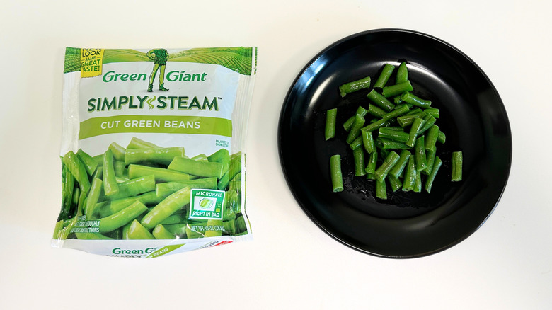 A black plate of green beans next to a bag of Green Giant Cut Green Beans