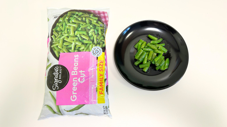 A black plate of green beans next to a bag of Signature Select Cut Green Beans