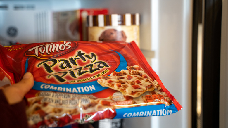 Hand holding Totino's Pizza Party in front of open freezer