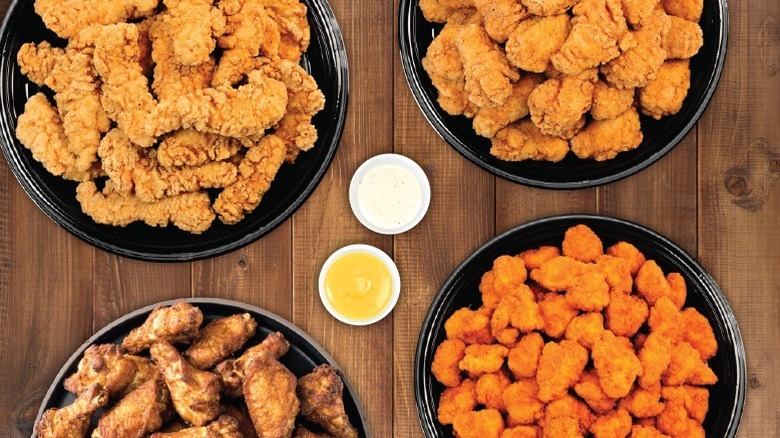 Overhead shot of 4 different types of chicken on platters with dipping sauce