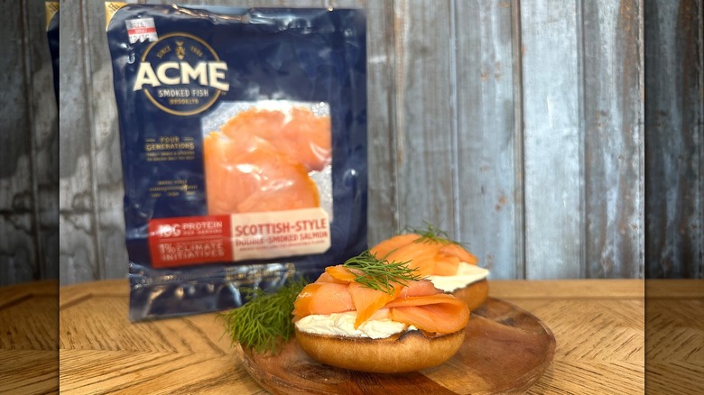 Acme brand smoked salmon on a bagel with dill and cream cheese in front of packaging