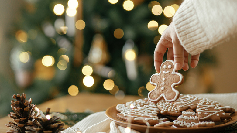 A hand reaches down to pick out a gingerbread man from a tray of cookies