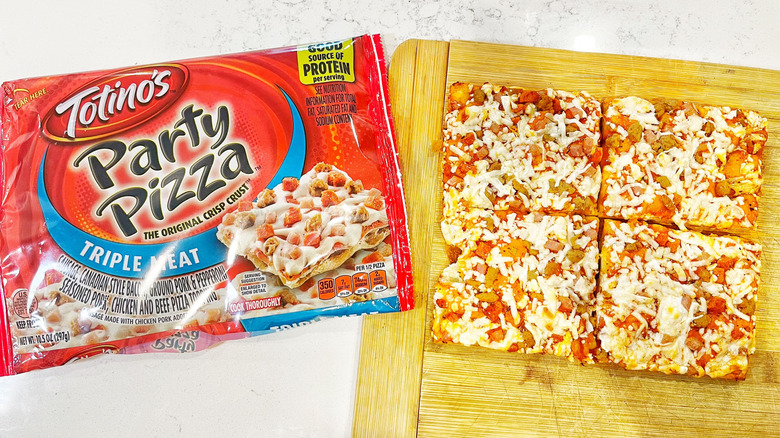 A Totino's Party Pizza baked on a cutting board next to its wrapper