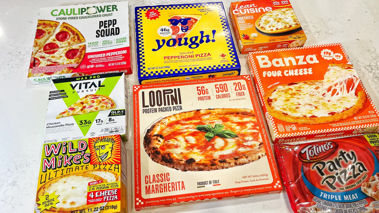 Eight different high-protein pizzas in their boxes on a marble countertop