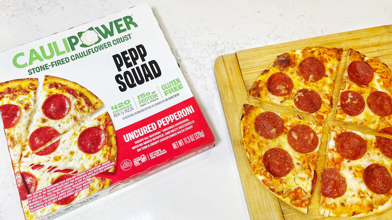 A Caulipower Pepp Squad pizza cut into quarters on a cutting board by its box