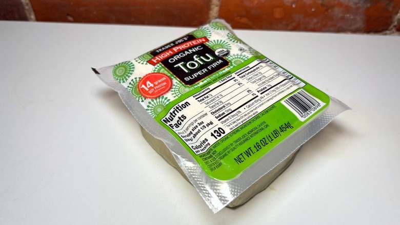 A green package of Trader Joe's Organic Tofu on a white countertop against a brick background