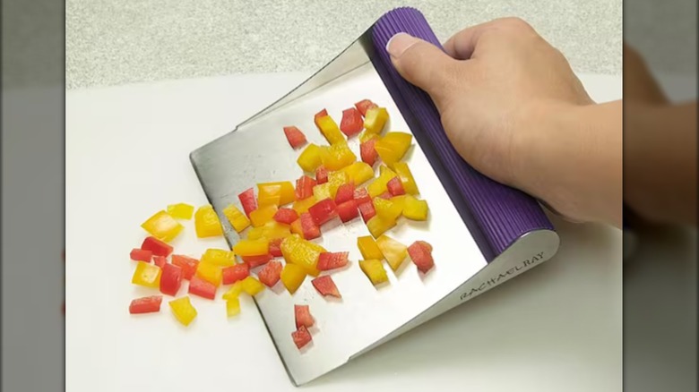 person using a scraper to pick up chopped veggies