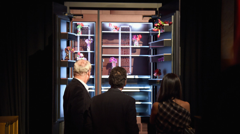 A photograph of a a JennAir fridge in a dark room with three people in front of it.