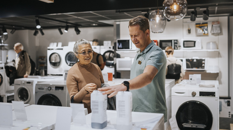 Tow people looking pointing at a dishwasher in a store.