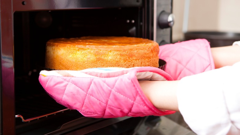 Hands with oven mitts taking a cake out of the oven