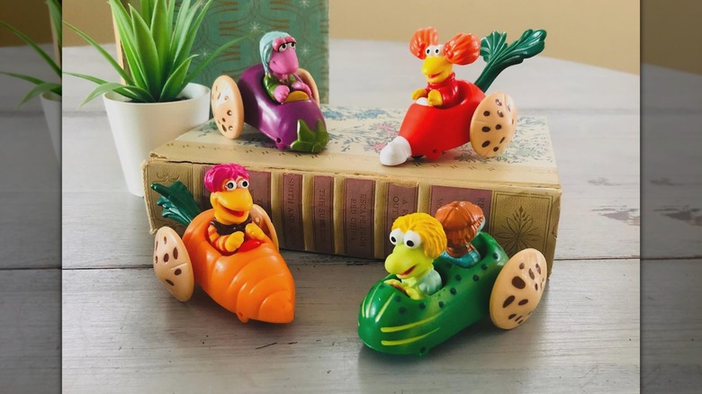 Four Fraggle Rock toys, with two on a book with a potted plant next to it