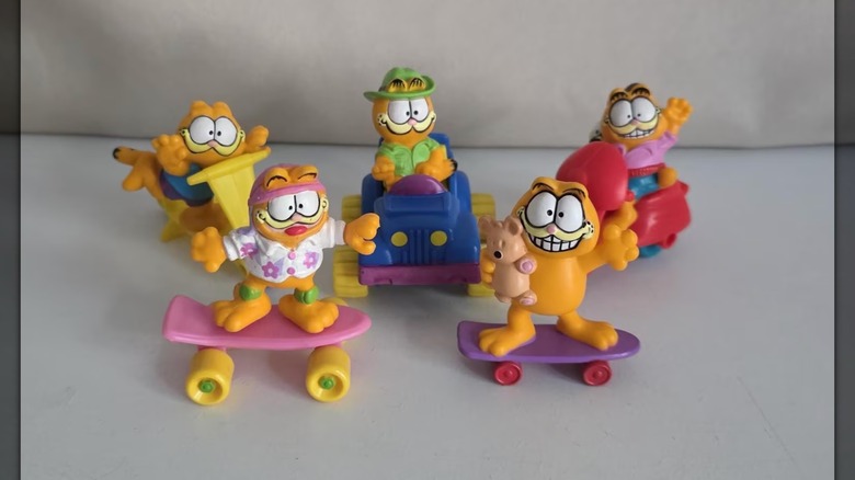 Several Garfield figurines on skateboards, scooters, and cars against a white background
