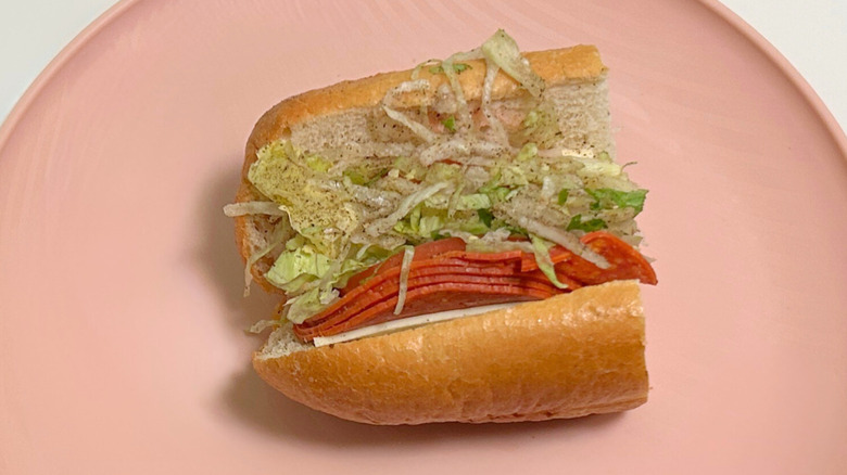 Close up of a small Wawa hoagie filled with lettuce and other toppings on a pink plate