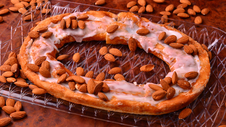 Almond danish kringle on a glass serving plate with almonds sprinkled around it