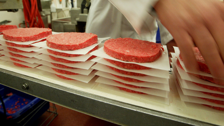 Stacks of raw burger patties separated by liners in a factory