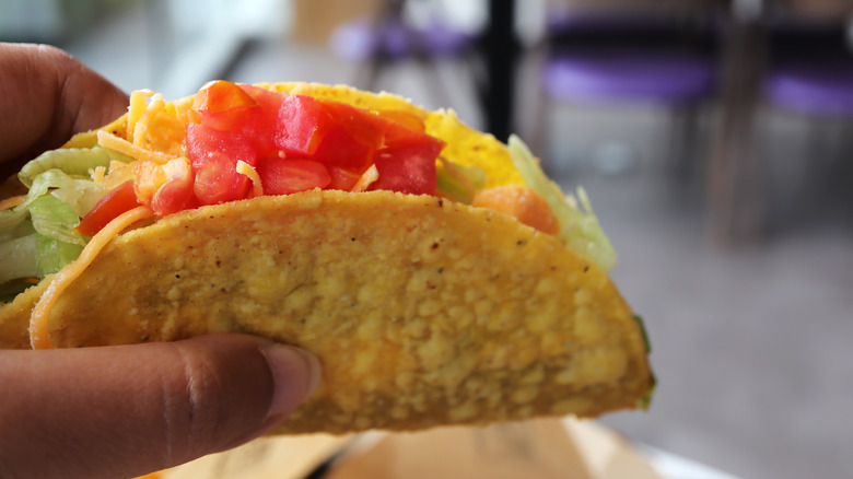Hand holding a crunchy taco filed with lettuce, cheese, and tomatoes