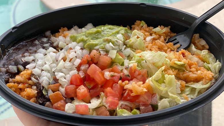 Hand holding Taco Bell veggie bowl in front of a pool